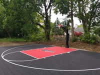Most of court, from front right corner toward hoop, in Brockton, MA. Small home court in black and red tile surface with custom logo designed from letters E and P.