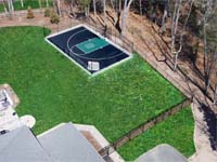 High overhead view at an angle of black basketball court with green key, G logo, and fencing in Canton, MA. Hockey net courtesy of resident youngster.
