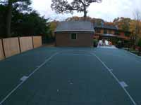 Chestnut Hill, MA transformation of a tight backyard space into a slate green basketball court with custom containment net fencing atop wooden fence.
