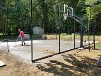 Small residential basketball court in Cranston, Rhode Island, featuring emerald green and sand tiles, and a custom Celtics logo. Shown here, washing dirt off the concrete base before installation of court surface, after fence posts and goal system are in place.