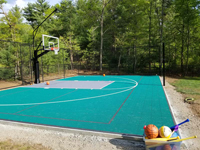 View down length of basketball court in Dover, MA, from left front end towrd right rear end, with box of plastic bats, toys, and basketballs prominent in foreground.