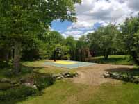Scenic, more distant view of olive green and yellow basketball court in Easton, MA, featuring lighting extension on goal system for night play.