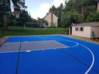 Residential backyard basketball court on asphalt in Massachusetts, in colorful blue and silver.