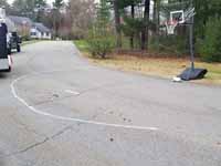 Home basketball court in Medway, MA, featuring royal blue and yellow Versacourt outdoor sport surface tiles. This is a view of the makeshift street court that the new installation replaces.
