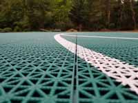 Green and red residential basketball court in Middleborough, MA. Closeup of white line also shows tile detail, designed for comfort and drainage.