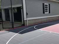 Milton, MA basketball court in a side yard, fit flush against a garage, featuring red and graphite Versacourt tiles.