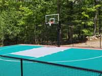 Residential backyard basketball court on fresh concrete base in stalled in Pepperell, MA, featuring fencing and an emerald green, titanium, and rust red sport tile surface.