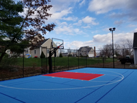 Angled view down length of blue and red basketball court from front left corner, showing dual lights on post against sky at right end of court, located in Shirley, MA.