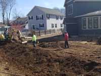 Photo from installation of a sand and emerald green residential backyard basketball court in Swampscott, MA. Before anything else, the way must be cleared for a lasting base. In this one, top soil and especially organic materials are being removed from the planned court site.