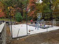 Graphite and titanium residential backyard basketball court in Westford, MA, with retaining wall, gated containment fence, and wood rail fence. Shown here during construction.