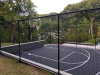 Side view of black basketball court through optional containment fence in Weston, MA.