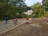 cement being poured and worked into one half of the base form for what will become a large emerald green and titanium backyard basketball court in Bolton, MA.