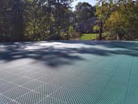Sun drenched view down part of large emerald green and titanium court in Bolton, MA, showing relative close-up of the tiles that make up the ergonomic, high performance surface.