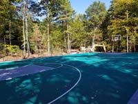 Long view at an angle of most of large emerald green and titanium backyard basketball court in Bolton, MA.