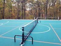 Commercial sized green residential basketball court in Bolton, MA features multiuse orange lines for pickleball, using a portable net shown here.