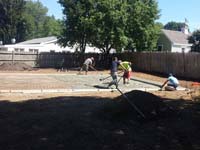 Pouring and working cement for sturdy concrete backyard basketball court base in Canton, MA.