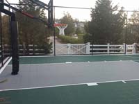 Home basketball court in Plymouth, MA, featuring hoop system, fencing, low impact green and grey outdoor sport tiles.