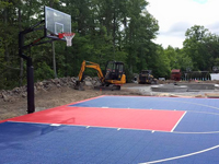 Focus on hoop end of blue and red North Attleboro court constructed alongside adjacent landscape work.