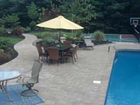View from a distance of how this green and burgundy multicourt in Kingston, MA fits seemlessly with the pool, hardscapes and beautiful landscape.