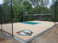 View from a near angle of overall sand and green basketball court, highlighting the optional net that makes it a multiple sport court, also featuring custom text and team logos, in Londonderry, New Hampshire.
