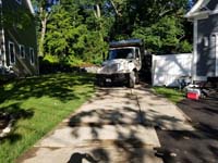 Driveway and part of front yard, showing protective measures taken during construction of slate green and titanium silver/grey basketball court in Needham, MA. Front view of dump truck shown above being loaded with grass and topsoil.