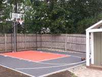 Very small graphite and rust basketball court with rebounder, taking advantage of unused corner of yard in Reading, MA.