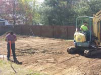 Digging up grass and ensuring an underlay free of organic matter before creating a foundation for a backyard basketball court in Sudbury, MA.