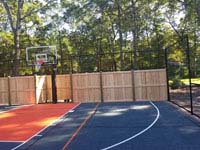 Graphite and orange residential basketball court in Walpole, MA, featuring custom cedar and rebound fence.