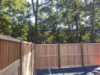 Corner view of custom wooden and mesh fence solution with graphite and orange home basketball court in Walpole, MA.