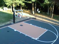 Focus on hoop system and key at one end of large Walpole, MA basketball court on blacktop underlay.