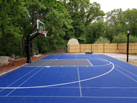 View of most of center court from front to back, with basketball hoop system and associated lines visible, along with center 'ice' hockey markings. Light and dark blue court in Burlington.
