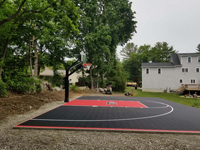 Longer view, from the left side, of black and red residential basketball court in Brockton, MA.