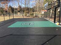 Residential basketball court in crisp black with a sharply contrasting green key and custom logo in Canton, MA.