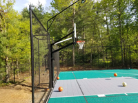 View down most of rear side, from left end of court, showing four basketballs positioned around ky, and showing the fence, goal system, and most of the court lighting system..
