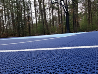 Distance photo from rear angle, showing complete blue resurfaced court in green grassy landscape in Marion, MA.