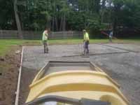 Emerald green and rust red home basketball court in Lynnfield, MA, featuring custom Celtics logo. Shown here spreading and smoothing cement being poured for a durable concrete court base.