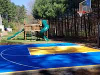 Home basketball court in Medway, MA, featuring royal blue and yellow Versacourt outdoor sport surface tiles.