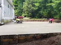 Milton, MA basketball court in a side yard, fit flush against a garage, featuring red and graphite Versacourt tiles. This picture shows the form and wet cement getting finishing touched before it turns to concrete.