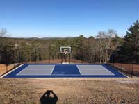 Multicourt for pickleball and basketball, fenced on three sides, on a hillside backyard in Plymouth, MA. Straight on image of completed court and scenic view down the hill beyond.
