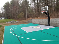 View from right end down length of home basketball court in Upton, MA, highlighting goal and containment netting with construction equipment in future parking lot beyond.