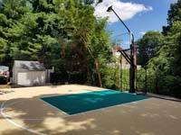 Angled view from front right toward goal of basketball court in Westwood, MA, showing off the lighting system above the hoop, and the fence around much of the court to keep the ball from wandering.