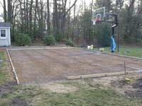 Form with rebard for pouring reinforced concrete base, shown with hoop already installed, for green and grey backyard basketball court installation in Agawam, MA.