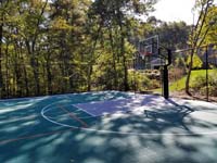 Closer view of one end of large emerald green and titanium backyard basketball court in Bolton, MA, showing off hoop system and containment fence.
