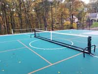 Portable pickleball net in place at center of pickleball lines on large emerald green and titanium backyard basketball court in Bolton, MA.