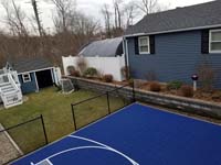 Context and detail of blue and grey small backyard basketball court with custom red H logo in Braintree, MA.