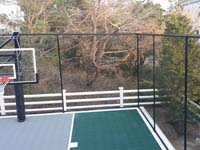 Focus on corner of home basketball court in Plymouth, MAshowing containment fence and hoop, as well as sport surfacec.