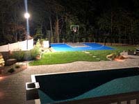 Blue and grey residential basketball court with custom Maximus logo under lighting in Walpole, MA.