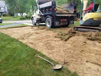 Removal of existing grass before building red and grey home basketball court in Groton, MA. Organic material must be removed, appropriate base material added and compacted, and a reinforced concrete base poured for maximum durability.