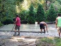 Workers shaping and smoothing cement for base of residential basketball court in shades of blue in Lexington, MA.