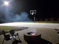 Preview of incomplete basketball court featuring Celtics logo, with fire pit, patio, and light for night play, in Londonderry, NH.